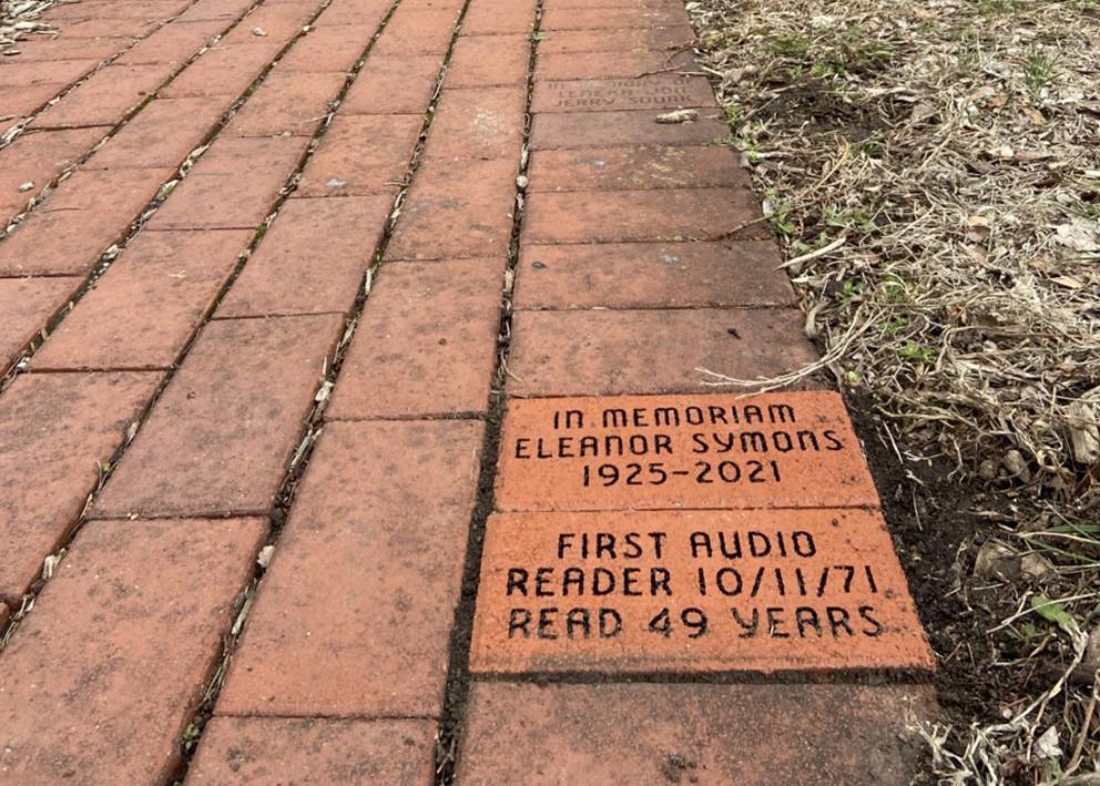 a closeup view of two of the sensory garden memorial bricks. one for Eleanor Symons 1925-2021  and the other is for audio reader's 49th anniversary
