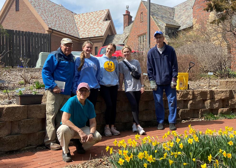 six volunteers stand in front of a patch of blooming daffodils