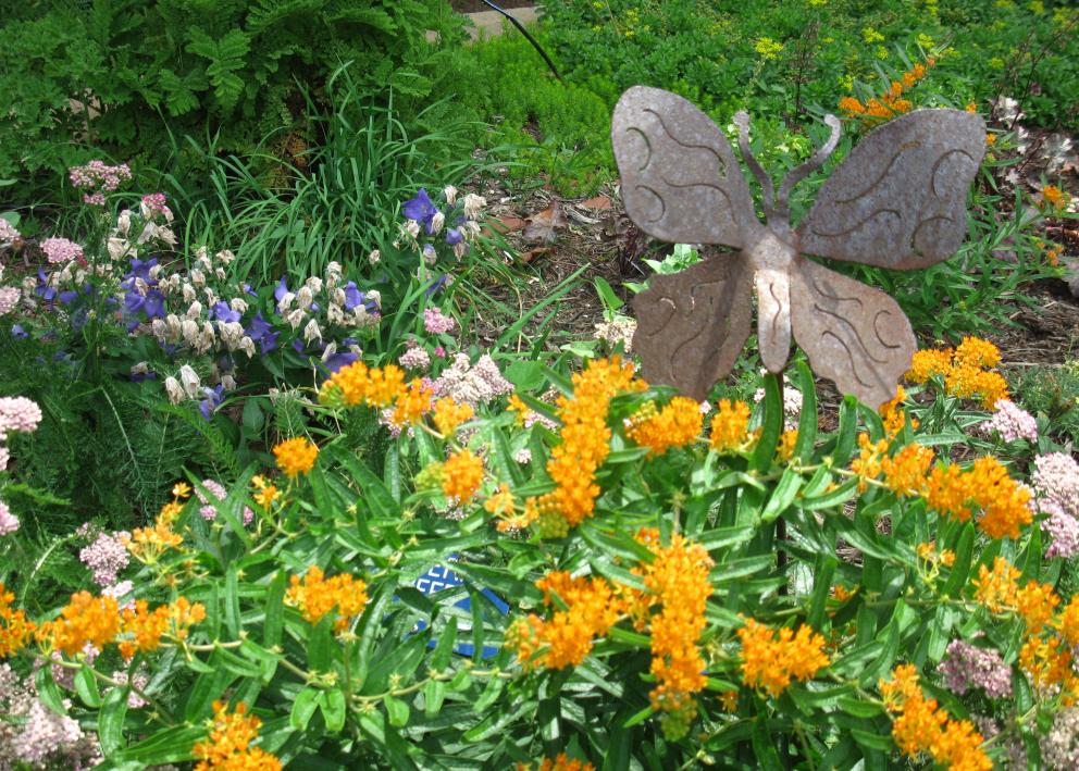 metal sculpture of a butterfly above colorful blooming flowers