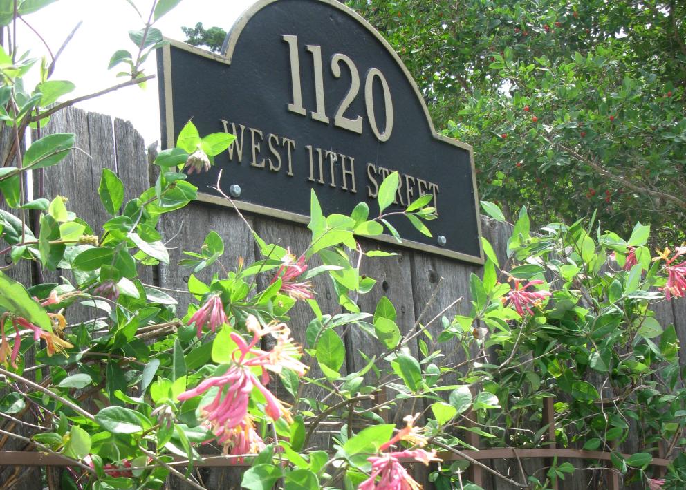 wooden fence with vines of pink flowers under the address sign which reads 1120 W 11th Street
