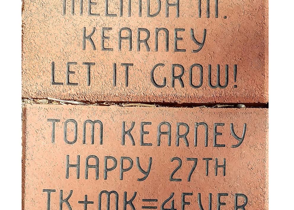 close up of Melinda and Tom Kearney's memorial bricks. Melinda's says "Let is Grow" and Tom's says "Happy 27th TK + MK = 4EVER"