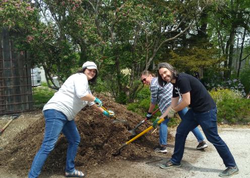 three people with racks around a large pile of mulch