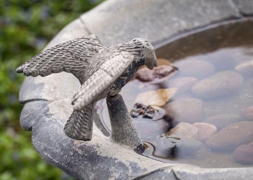 stone birdbath with a small bird statue with open wings perched on the edge