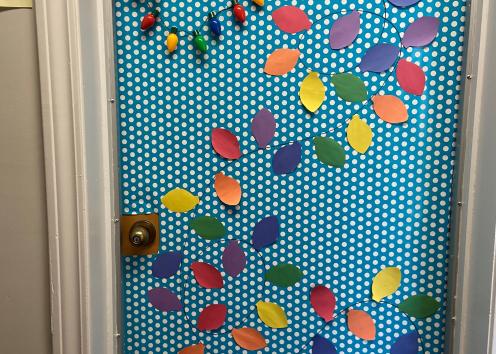Door number 10 is adorned in blue and white polka-dot paper with a strand of Christmas lights made out of construction paper cascading down the door. At the top of the door is a Santa Hat and a small strand of real lights.