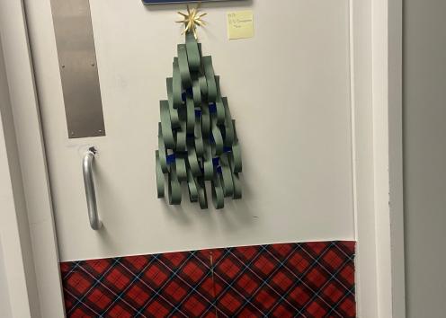 Door number thirteen features a 3-D Christmas tree made out of construction paper. The bottom of the door is covered in red, plaid wrapping paper with gold ribbon, made to look like a wrapped present. 