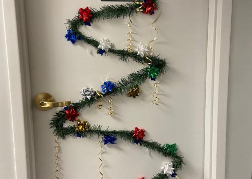 Door number four features a large Christmas tree made out of evergreen garland, various colored present bows, and gold curly ribbon.