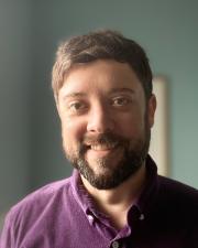 a smiling man with brown hair, a trimmed beard, and short hair