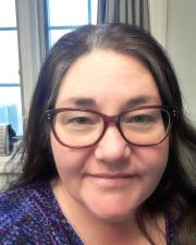 closeup of smiling woman with long dark hair with silver streaks smiling and wearing rimmed glasses